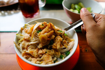 Typical Semarang soto ayam or chicken soto, with clear soup, suitable for breakfast, lunch or dinner. popular food in Indonesia. With fried garlic topping served in small bowl on wooden table.