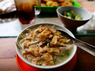 Typical Semarang soto ayam or chicken soto, with clear soup, suitable for breakfast, lunch or dinner. popular food in Indonesia. With fried garlic topping served in small bowl on wooden table.