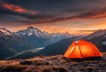Glowing orange tent camping in the mountains in front of majestic mountain range