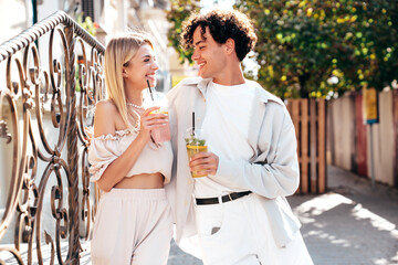 Young smiling beautiful woman and her handsome boyfriend in casual summer clothes. Happy cheerful family. Female having fun. Couple posing in street. Holding and drinking cocktail drink in plastic cup