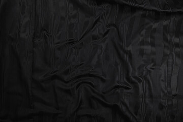 Texture of black taffeta (silk) fabric with black stripes pattern, top view. Background, texture of draped dressy fabric with shining black stripes pattern.