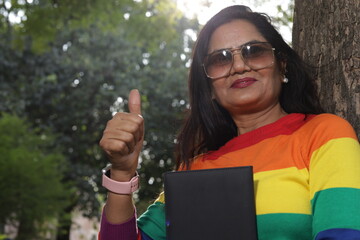 Portrait of mid aged woman holding a black color almanac in hand, sunlight, green park serene...
