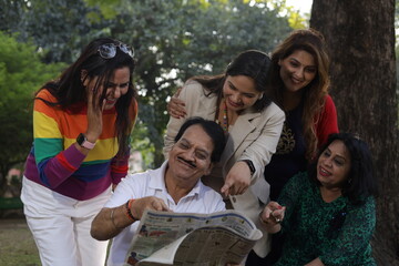 Obraz premium Reunion of happy Indian friends. green park lush green atmosphere. tranquil and serene environment. elderly old friends together. everyone in park reading a newspaper and having fun in day time.