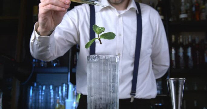 Super slow motion macro of falling fresh aromatic leaf of peppermint herb falling in transparent glass with soda and ice cubes during mojito cocktail preparation by bartender in bar or restaurant.
