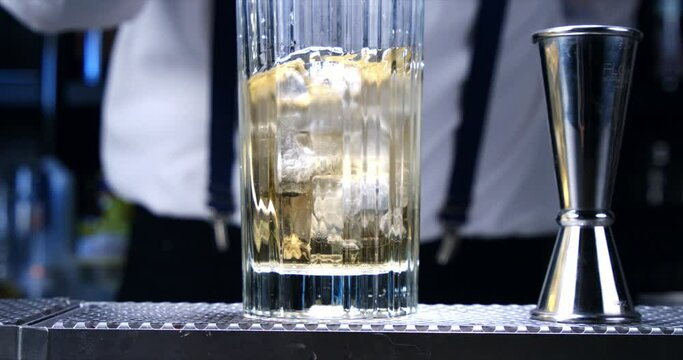 Super slow motion macro of fresh cool crystal ice cubes being put in transparent glass by bartender during preparation of alcoholic cocktail to customers at the bar or disco club at 1000 fps.