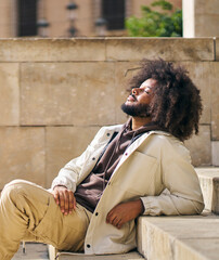 Portrait of a man with afro hair sitting on a step in the square