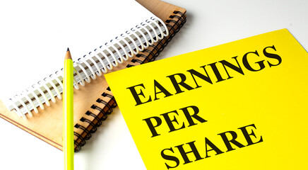 EARNINGS PER SHARE text on yellow paper with notebooks
