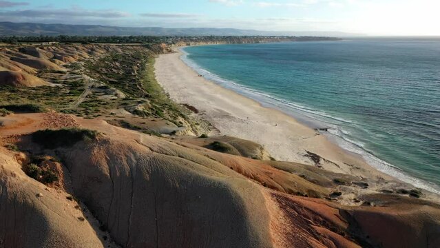 Aerial view of a white sandy beach being revealed from behind a rocky summit, Port Willunga, South Australia, Australia
