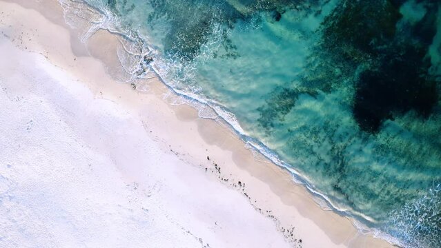 Aerial view of blue crystal clear water and waves rolling onto a white sandy beach, filmed from above, Port Willunga, South Australia, Australia
