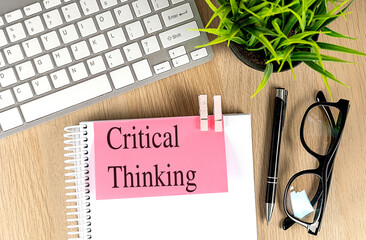 CRITICAL THINKING text pink sticky on notebook with keyboard, pen and glasses