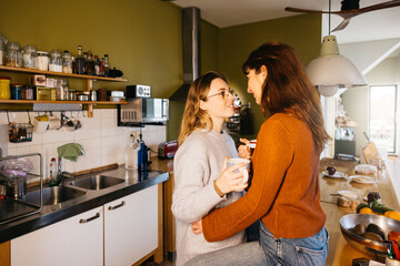 Young female couple sharing a cup of tea in their home kitchen. Lesbian couple enjoying a moment together, sipping tea in the comfort of their home kitchen.