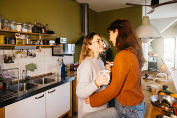 Young female couple sharing a cup of tea in their home kitchen. Lesbian couple enjoying a moment...