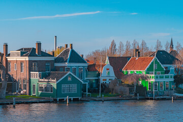 Beautiful Dutch scenery panorama of Zaanse Schans village in Netherlands in spring time. Ancient houses brightly colored at the water's edge against a blue sky in sunny weather