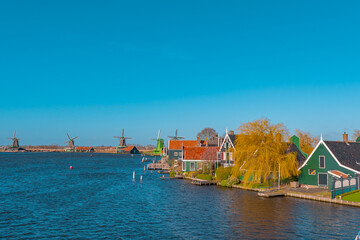 Naklejka premium Beautiful Dutch scenery panorama of Zaanse Schans village in Netherlands in spring time. Ancient windmills at the water's edge in the background with the blue sky in sunny weather