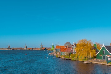 Fototapeta na wymiar Beautiful Dutch scenery panorama of Zaanse Schans village in Netherlands in spring time. Ancient windmills at the water's edge in the background with the blue sky in sunny weather