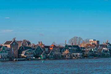 Beautiful Dutch scenery panorama of Zaanse Schans village in Netherlands in spring time. Ancient houses brightly colored at the water's edge against a blue sky in sunny weather