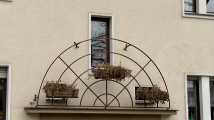 Decorative protective grille with three flower boxes. A lattice in the shape of semicircles intersected by lines. Narrow window, beige wall, plastered.