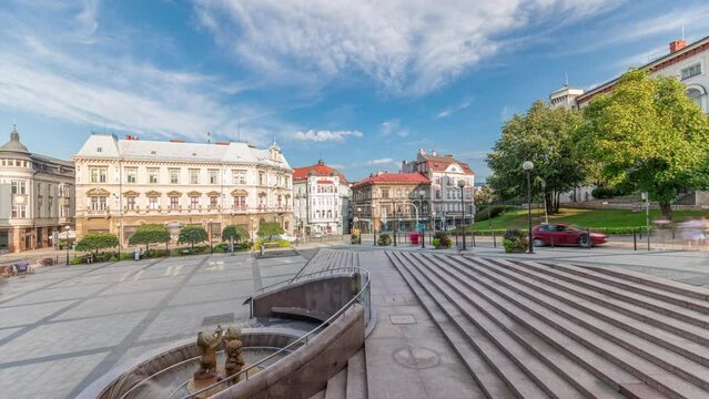 Panorama showing Sulkowski Castle and fountain on Chrobry Square in Bielsko-Biala timelapse, Poland. Historic buildings around. People walking and sitting in cafe. Clouds on a blue sky