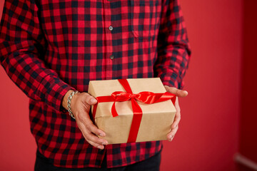 Close-up of hands holding a gift box with a red ribbon against a red background.