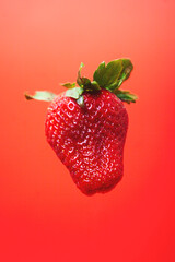 Delicious ripe strawberry floating on a red background.