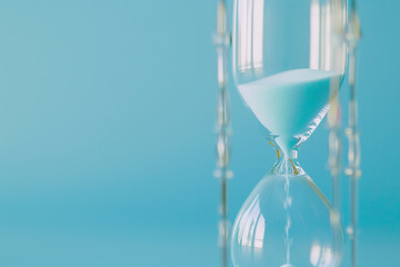 close-up shot of an hourglass against a minimalist blue backdrop, capturing the quiet intensity of time slipping away as deadlines approach - obrazy, fototapety, plakaty