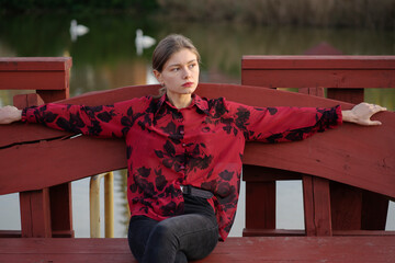 Portrait of a young girl sitting in a park on a bench near a lake
