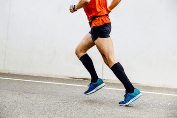 side view man running in black compression socks in background white concrete wall