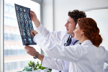 Doctors, brain scan and reading for results at hospital with pointing, teamwork and health by window. Neurologist, partner and medic with mri for wellness, check and decision with document in clinic - obrazy, fototapety, plakaty