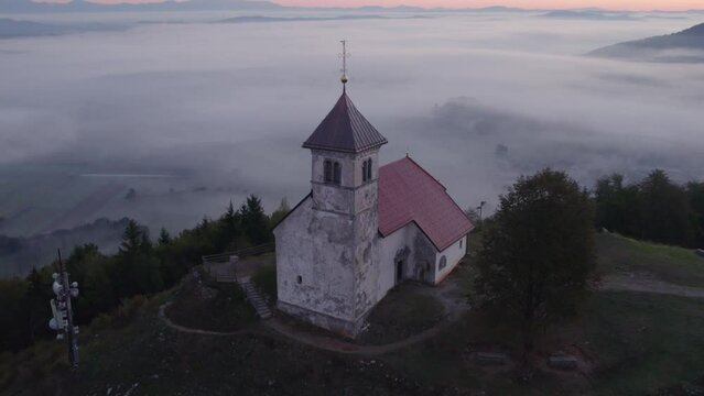 Aerial view of St. Anne's Church (Cerkev sv. Ane) on top of a mountain with low fog, Jezero, Slovenia