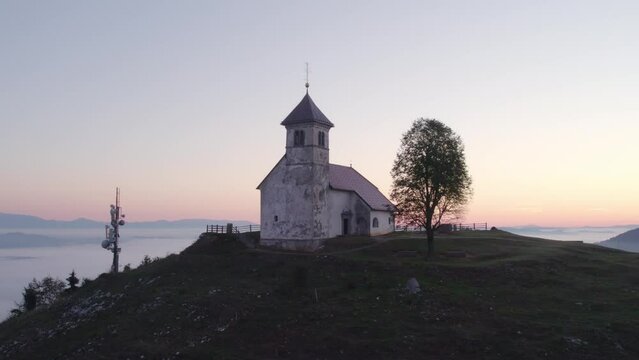 Aerial view of St. Anne's Church (Cerkev sv. Ane) on top of a mountain with low fog, Jezero, Slovenia