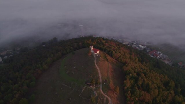 Aerial view of St. Anne's Church (Cerkev sv. Ane) on top of a mountain with low fog, Jezero, Slovenia
