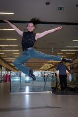 The young and talented teen dancer jumps and makes a gracious pose in the air in a shopping mall indoor