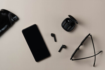 Black accessories on beige background. Phone, headphones, glasses