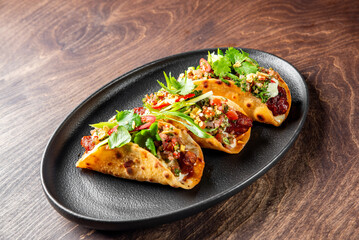 Delicious tacos with fresh vegetables and meat on a black plate, garnished with herbs.