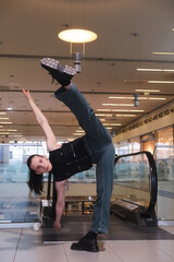 A young androgynous teenage male dancer doing acrobatic dancing poses indoors in a shopping center