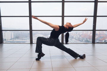 A young androgynous teenage male dancer doing acrobatic dancing poses indoors in a shopping center