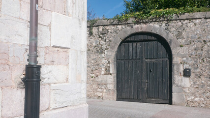 Puerta de madera con arco en muro de piedra en Llanes