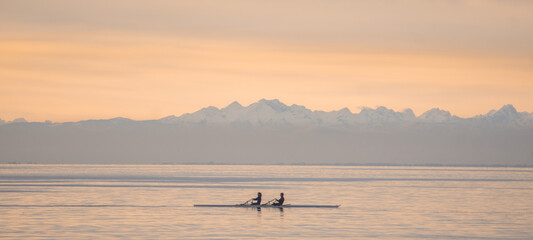 Two canoeists on one canoe sailing on the gulf of Trieste with the beautiful Alps in the background all at sunset