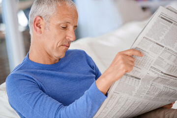 Senior, man and reading a newspaper on sofa for article, information and morning routine in living...
