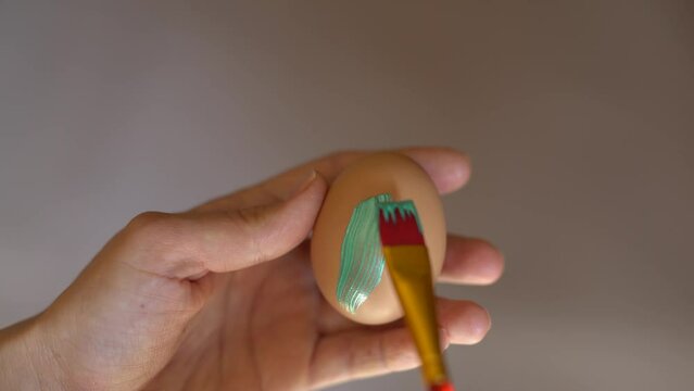Close-up of a hand painting on an egg with a brush. Easter tradition of painting eggs. Egg symbol of Easter.