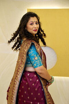 Gujarati woman wearing Saari in Gujarati stlye. Model is posing with a side pose and have smiling face and cirly hair. she has wore bindi and lovely bangles. Green and purple saari is just beautiful