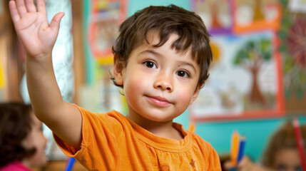 A young boy raises his hand in a classroom, eager to participate in the learning process