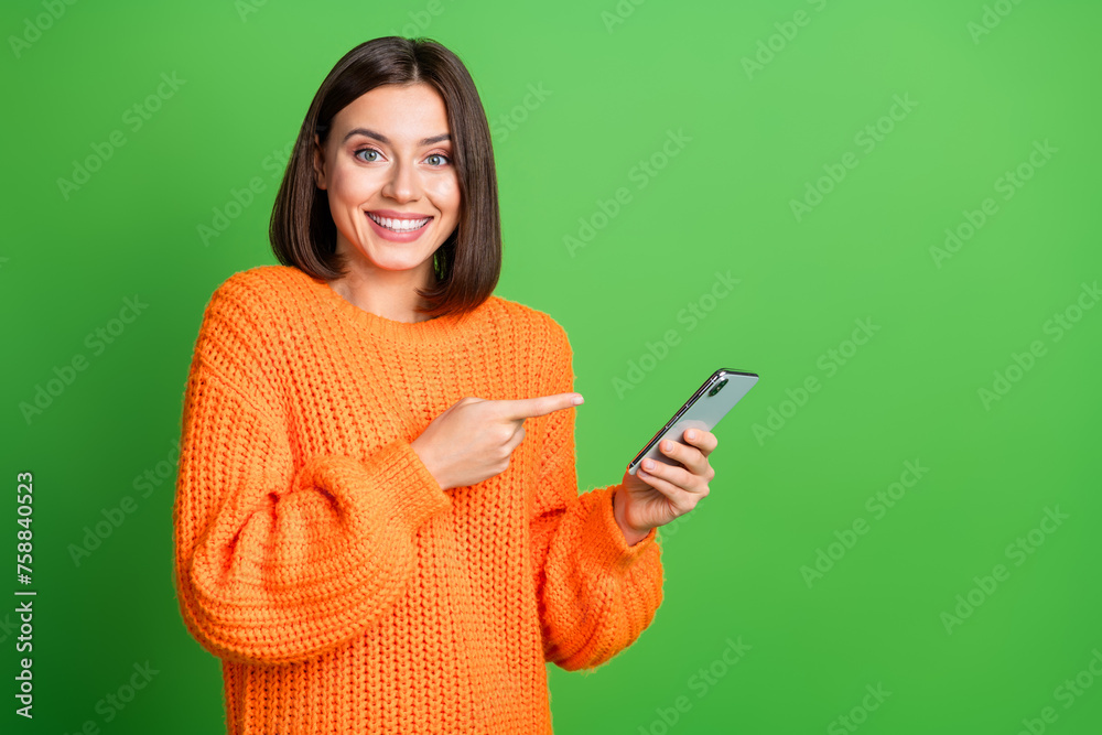 Sticker Portrait of cheerful charming person toothy smile indicate finger hand hold smart phone empty space isolated on green color background