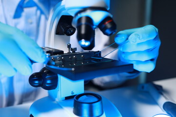 A talented scientist sits in his lab while using a microscope to look for microscopic organisms in...