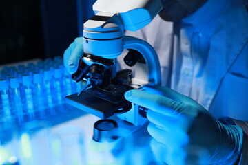 A talented scientist sits in his lab while using a microscope to look for microscopic organisms in...