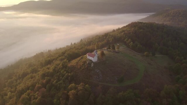 Aerial view of St. Anne's Church (Cerkev sv. Ane) on top of a mountain with low fog, Jezero, Slovenia
