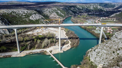 Construction of a high bridge over the river, aerial drone view. Workers and machines on...