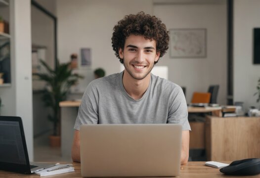 A curly-haired man working at his laptop with a smile, in a home office. His demeanor is relaxed yet productive.