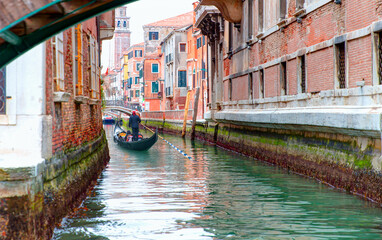 Venetian gondolier punting gondola through green canal waters of Venice Italy - obrazy, fototapety, plakaty
