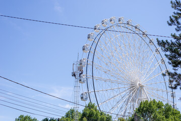 Workers on a communication tower by a ferris wheel in white color against summer blue sky